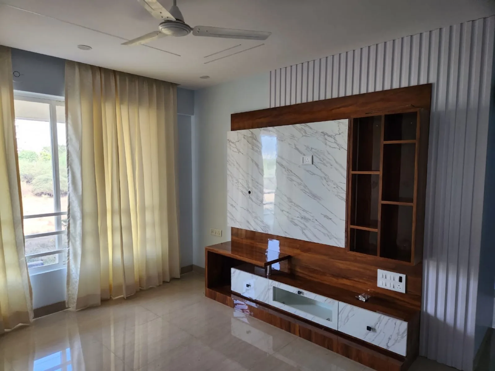 Living room feature wall in a Pune flat with fluted wood panelling and a marble-finish panel behind a wall-mounted TV